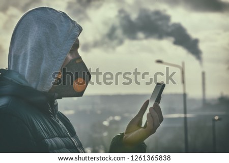 Man wearing a real anti-pollution, anti-smog and viruses face mask and checking current air pollution with smart phone app Royalty-Free Stock Photo #1261365838