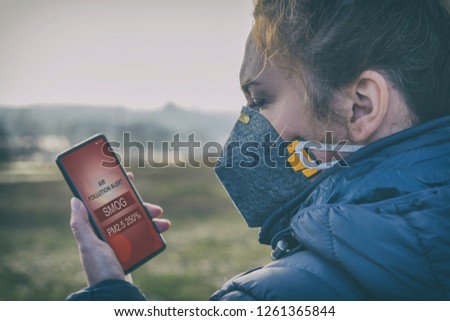 Woman wearing a real anti-pollution, anti-smog and viruses face mask and checking current air pollution with smart phone app Royalty-Free Stock Photo #1261365844