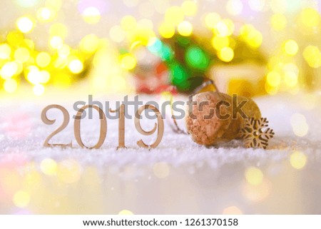 Champagne stopper in the snow with wooden digits 2019 and a snowflake. Christmas card in bright Golden lights