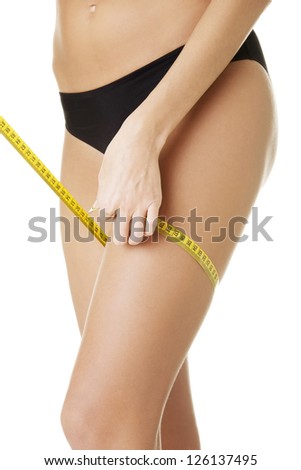 Closeup photo of a Caucasian woman's leg. She is measuring her thigh with a yellow metric tape measure after a diet