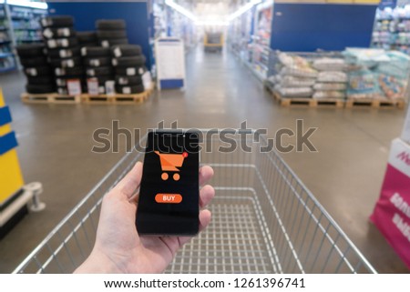 Shopping basket on a mobile phone screen. Button Buy. Hand holding mobile phone on Supermarket blur background.
