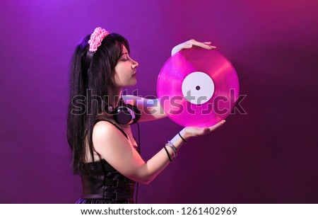 Young DJ woman with pink vinyl enjoys music. Glamorous girl with headphne on purple background plays music disko.