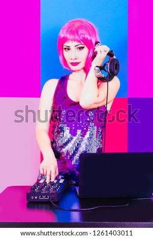 Glamorous DJ girl with pink hair and headphne on red, pink and blue background plays music disko.