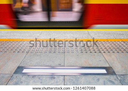 blurred red subway train, tactile paving also called detectable warning surfaces for visually impaired. yellow line, safety warning lamp