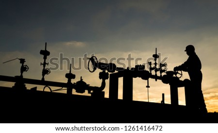 Silhouette of the oilfield worker monitoring the manifold valves in the oilfield  Royalty-Free Stock Photo #1261416472