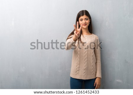 Teenager girl with sweater on a vintage wall happy and counting three with fingers