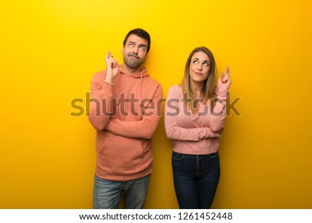 Group of two people on yellow background with fingers crossing and wishing the best