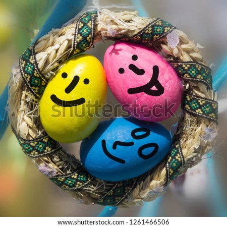 three Egg faces are around some easter eggs.