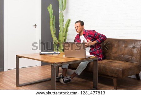 African american man with laptop in the living room having a pain in the heart