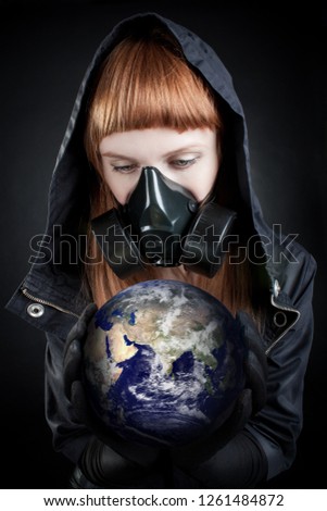 Girl in hood holding earth in her hands over dark background.  Photos of the earth made by NASA 