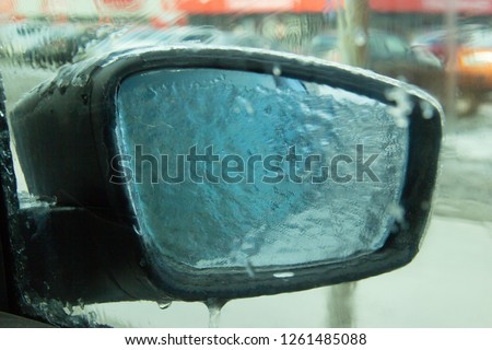 Picture of an iced car mirror and window. Photographed from inside the cabin through a frozen window. Blurred