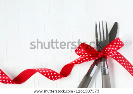 Fork and knife tied with a red ribbon on white background with copy space. Food, restaurant and table setting theme, copy space