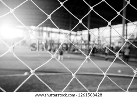 black and white picture of White mesh goal with blurry young boy soccer players sitting with coach on artificial turf.