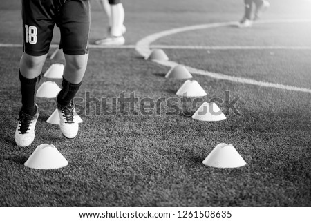 black and white picture of soccer player Jogging and jump between cone markers on artificial turf for soccer training. Football or Soccer Academy.