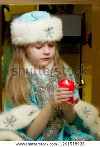 A nice little girl in a New Year's suit is holding a candle. The concept of a Christmas family holiday, children's emotions.