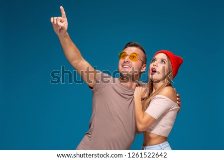 Surprised couple in casual clothes pointing with their index fingers up looking there with great astonishment isolated over blue background