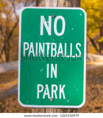 Green no paintballs in park sign on wooden pole