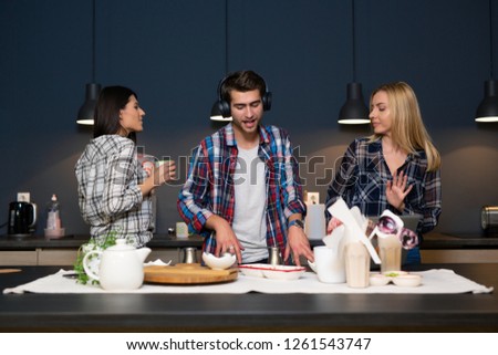 Man pretending to be a DJ in the kitchen with two girls dancing with him. Friends having good time