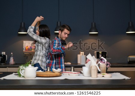 Man pretending to be a DJ in the kitchen with his girlfriend while dancing and singing with her. Friends having good time