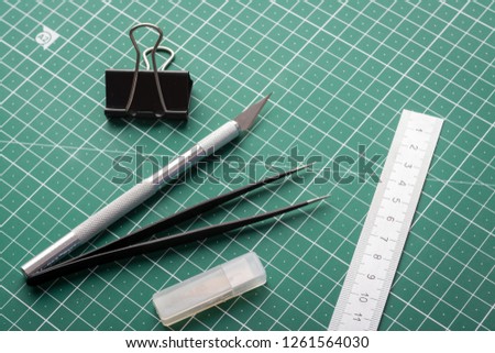 Scalpel, tweezers, ruler, paper clip and box with blades for knife on cutting mat