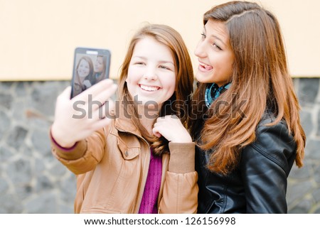 Two teen girls taking selfshot or selfy picture of themselves using tablet computer outdoors portrait