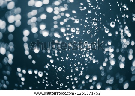 Dirty window glass with drops of rain. Atmospheric blue background with raindrops in bokeh. Droplets and stains close up. Detailed transparent texture in macro with copy space. Rainy weather.