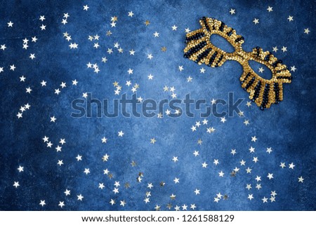 Golden glittering mask with golden stars on blue background. Top view, copy space. Carnival party celebration concept