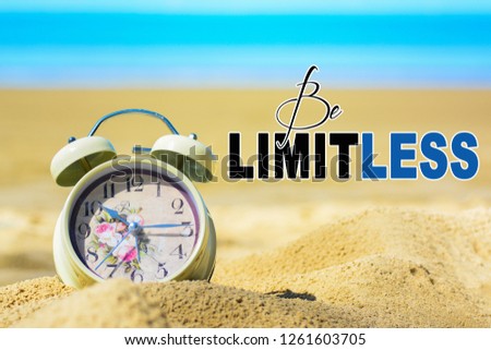 A retro alarm clock on a sand at the beach with blue sea background. A text 'Be limitless' written on image.