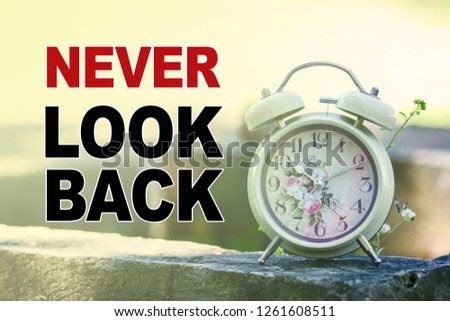 A retro alarm clock in the morning light with nature background. A text 'Never Look Back' written on image.