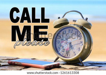 A retro alarm clock and a mobile phone on a stone floor at the beach with blue sea background. A text 'Call Me Please' written on image.