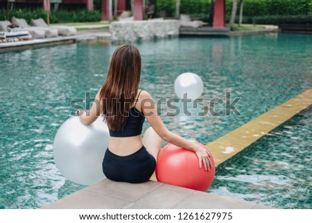 beautiful smiling asian woman in bikini and sunglasses holding inflatable ball at poolside