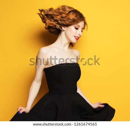 portrait of beautiful woman with blond curly hair in black dress over yellow background