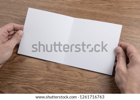 Mens hands holding empty white booklet on wooden background. View from above