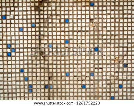An old cracked wall covered with mosaic tiles, close up view. White and blue mosaic tiles pattern. Abstract background. Vintage wall with tiles texture. Ancient masonry surface