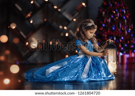 Happy cheerful little girl excited at Christmas Eve, sitting under decorated illuminated Christmas Tree. Greeting card or cover, horizontal with copy space.