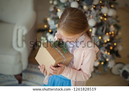 A pretty happy brown-haired girl is holding gifts at the Christmas tree. New year and Christmas.