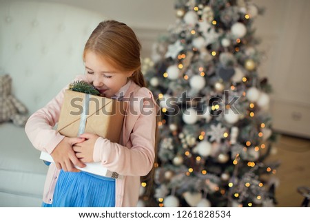A pretty happy brown-haired girl is holding gifts at the Christmas tree. New year and Christmas.