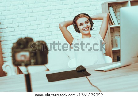 Blogger Makes a Video. Blogger is Gamer. Blogger is Smiling Woman. Camera Shoots a Video. Woman in Headphones Playing a Video Game on Computer. Resting Woman Looking into a Camera. Studio Interior.