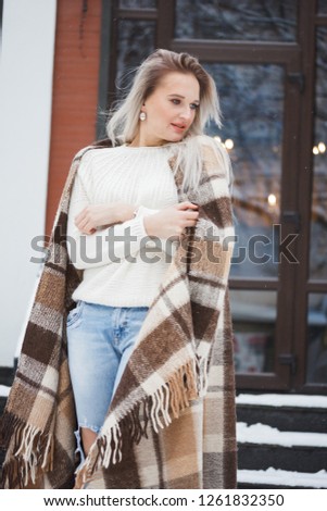Beautiful natural young smiling shy friendly blonde woman wearing knitted sweater on a grey background.