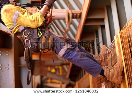 
Wide angle view picture of male rope access inspector worker wearing full safety harness setting on a chair, abseiling performing wall inspection working at height construction site, Sydney, Austral