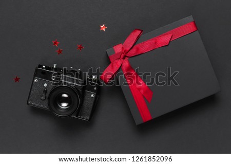 Old retro vintage camera, Black gift box with red ribbon on black background top view flat lay with copy space. Concept for the photographer, old photographic equipment, minimalistic style