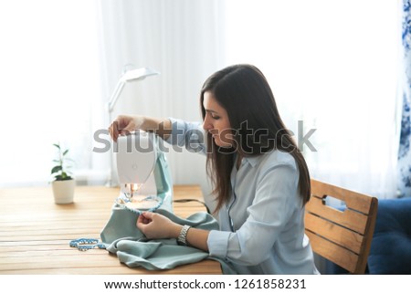Charming girl with long black hair sews on a sewing machine, concept handmade and mother on maternity leave. Real workshop