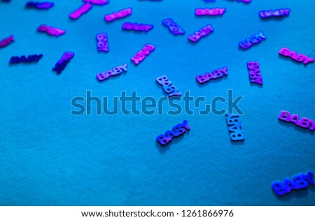 Neon colored confetti with words baby scattered on blue background with copy space. Modern trendy baby shower template for invitations, greeting cards, banners, albums