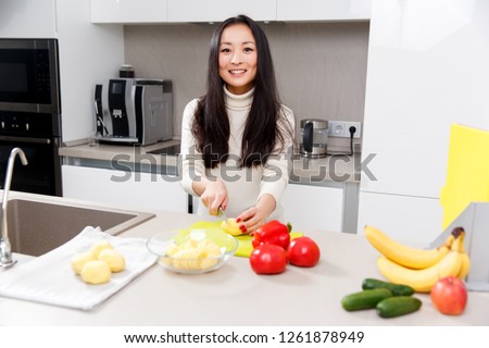 Picture of happy brunette cutting potatoes at table with vegetables and fruits