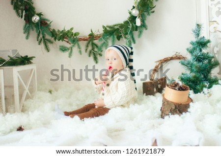 Little cute baby with blond curly hair in a knit cardigan and a warm hat in the Christmas decorations

