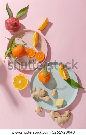 Fresh juicy tangerines, pomegranates and sliced fruits on colored plates on a pink background. Summer mood, healthy food. Top view.