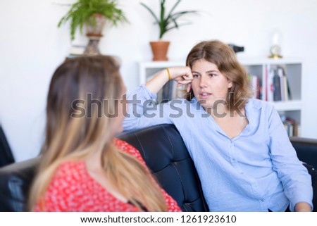 Two friends talking and laughing on a sofa in the living room at home