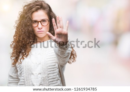 Beautiful brunette curly hair young girl wearing winter sweater over isolated background doing stop sing with palm of the hand. Warning expression with negative and serious gesture on the face.