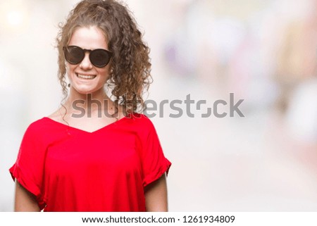 Beautiful brunette curly hair young girl wearing sunglasses over isolated background with a happy and cool smile on face. Lucky person.