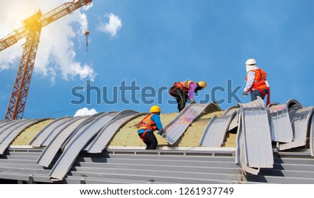 construction workers to roofing metal sheet on high places on large building in construction site Royalty-Free Stock Photo #1261937749